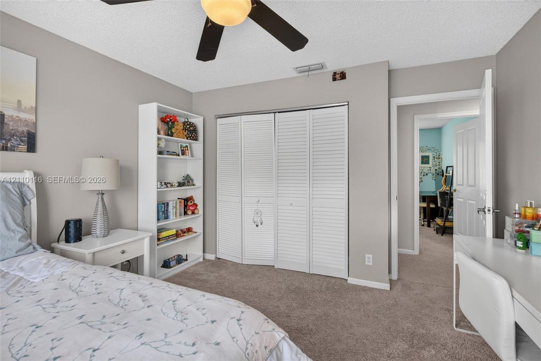 Bedroom featuring wall-to-wall carpeting, ceiling fan with integrated lighting, built-in shelving, and white louvered-style closet doors