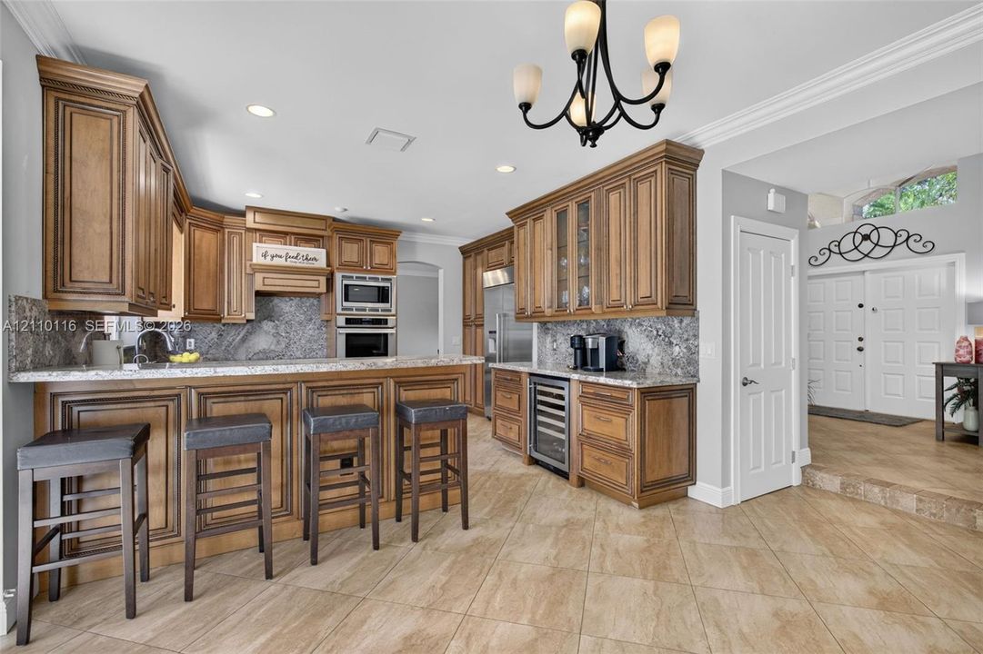 Kitchen featuring custom raised-panel wood cabinetry, stone countertops, integrated beverage refrigerator, recessed lighting, and a multi-arm chandelier
