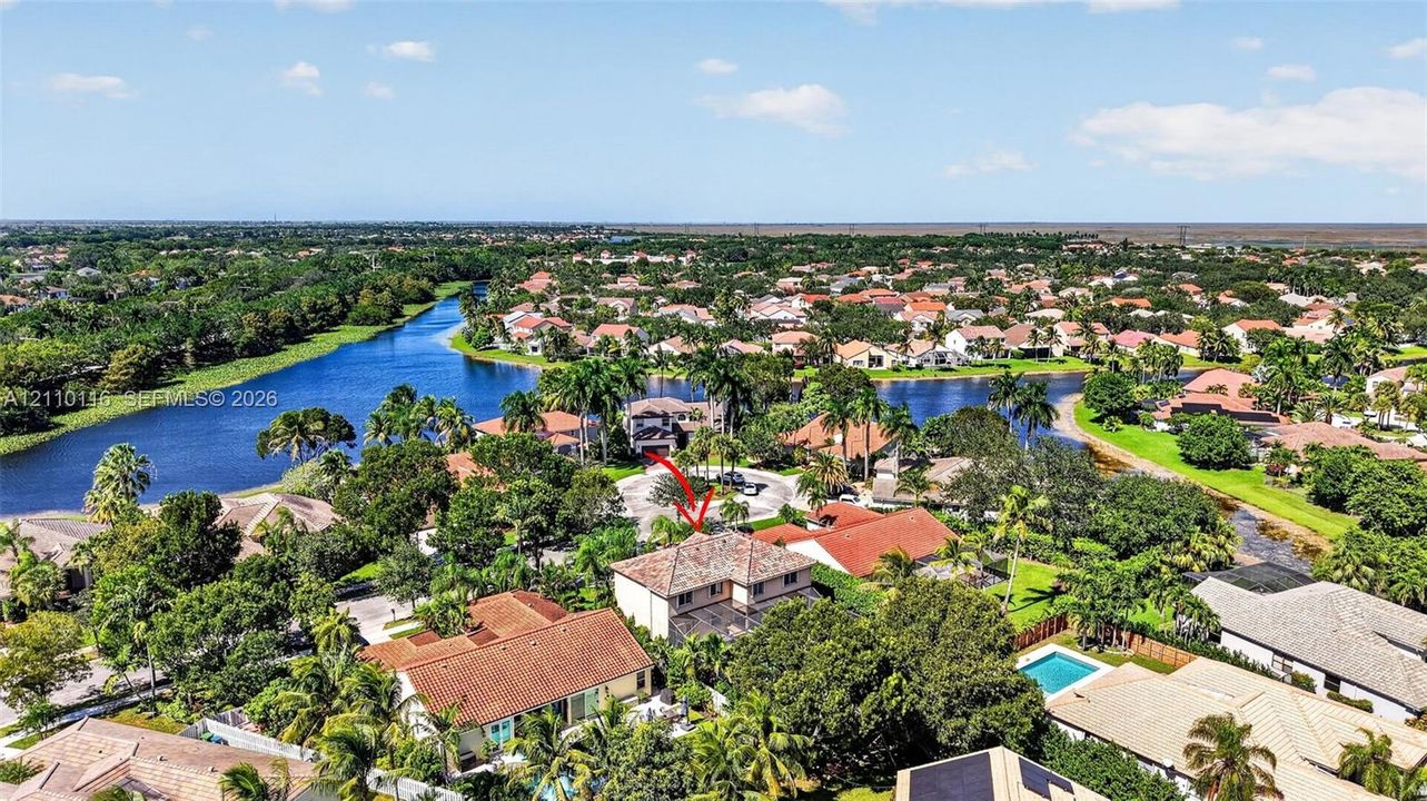 Aerial perspective of property featuring a multi-story residence with a tile roof, situated in a community with expansive water frontage and mature landscaping