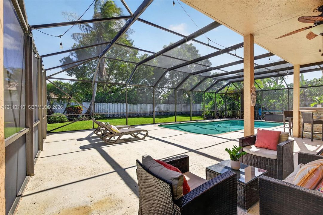Screen-enclosed patio featuring a concrete deck, built-in outdoor bar, recessed ceiling fan, and swimming pool
