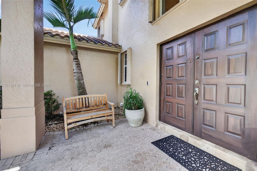 Stucco exterior entrance featuring a double-door entry with raised panel detailing, concrete paver flooring, and a tiled roofline