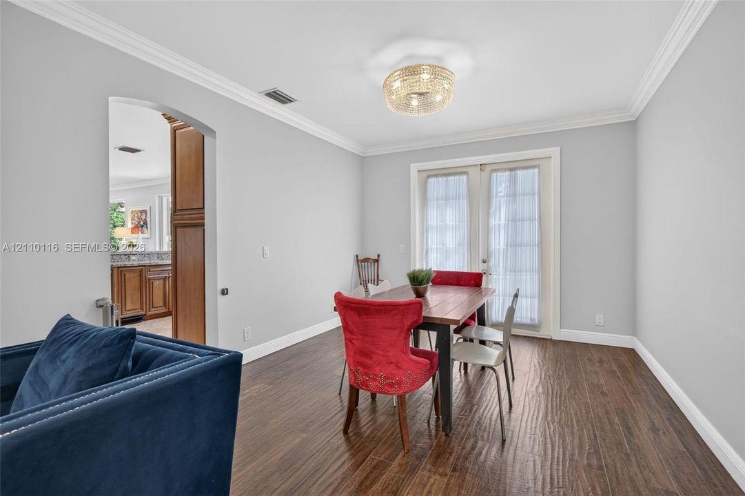 Wood-finish flooring, crown molding, a decorative circular flush-mount light fixture, and French doors