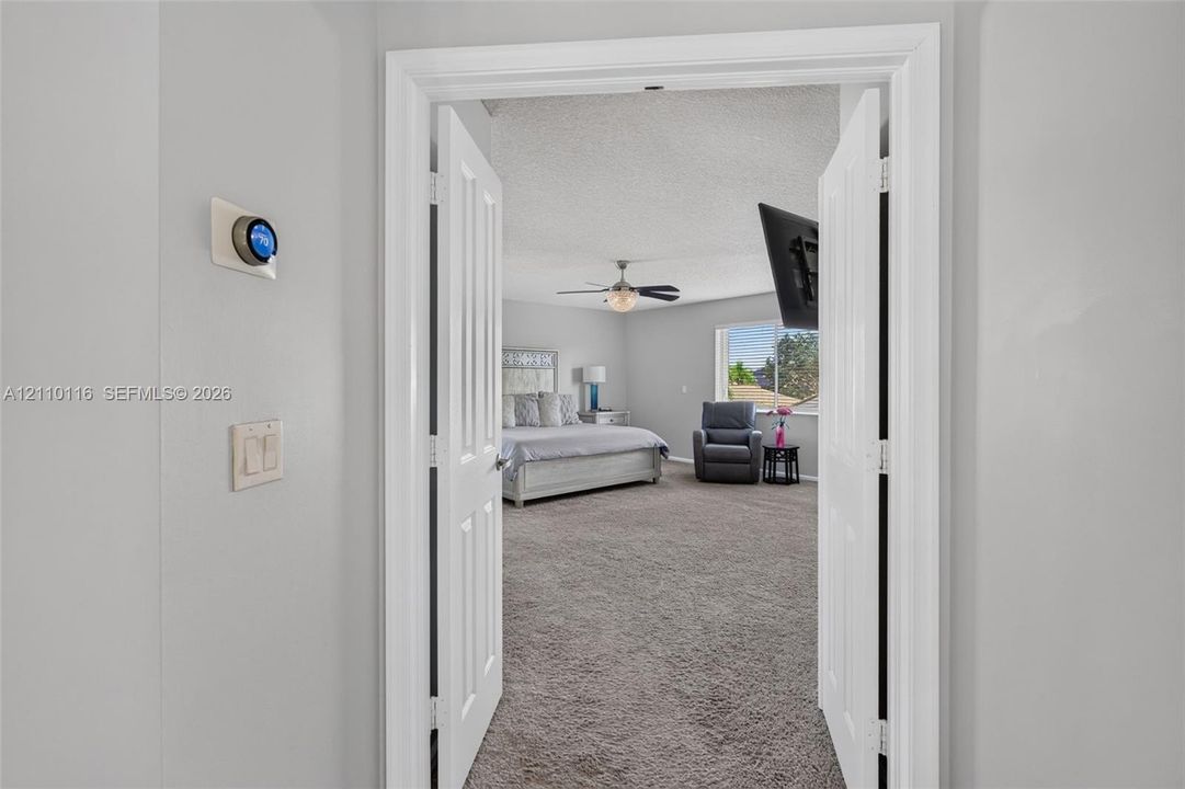 Double door entrance featuring wall-mounted smart thermostat, carpeted flooring, ceiling fan with integrated lighting, and dual-pane window