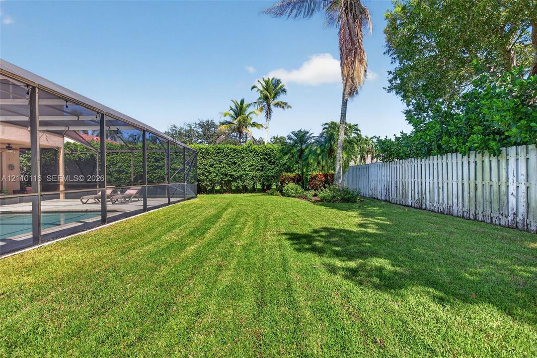 Private backyard featuring a screened-in pool enclosure, manicured lawn, established perimeter hedges, and a vertical wood privacy fence