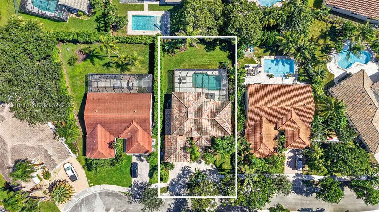 Aerial view of property featuring a tile roof, screen-enclosed pool, landscaped lawn, and paved driveway