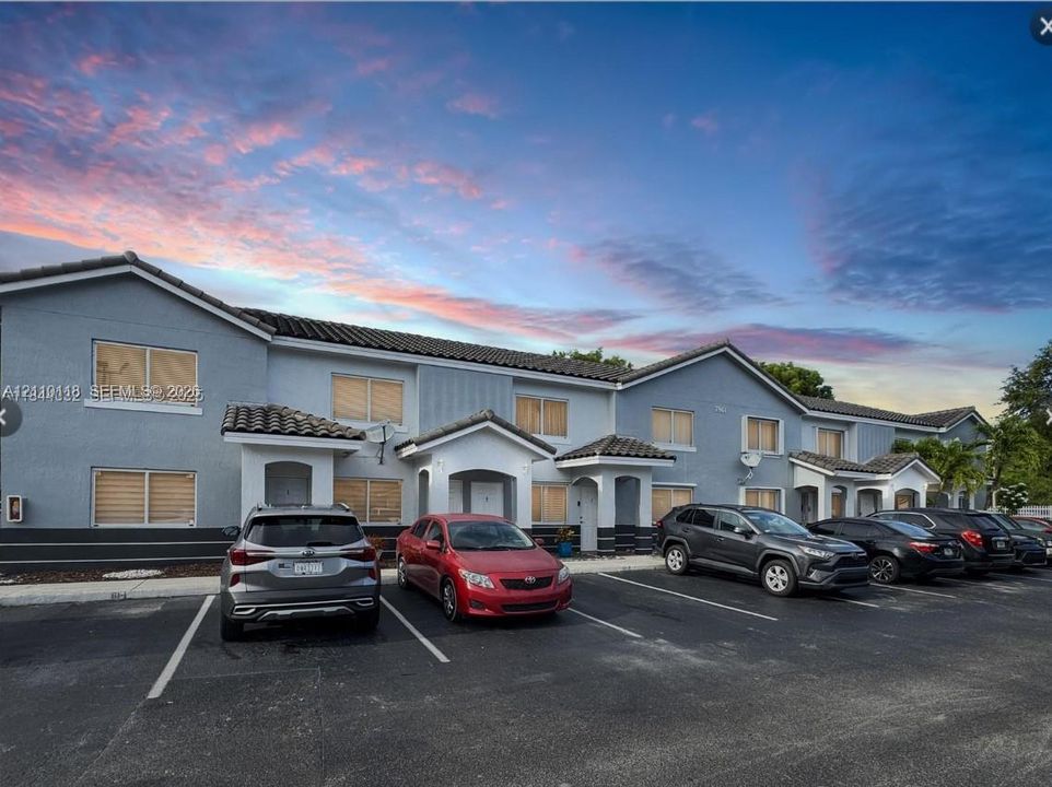 Multi-family structure with stucco exterior, clay-tile roofline, covered entryway gables, and dedicated surface parking