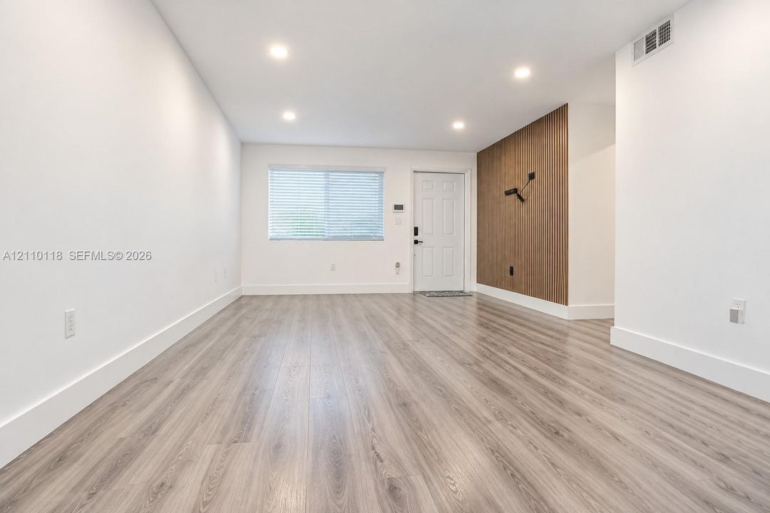 Interior space featuring wood-finish flooring, recessed lighting, and a vertical wood-slat accent wall with a wall-mounted light fixture
