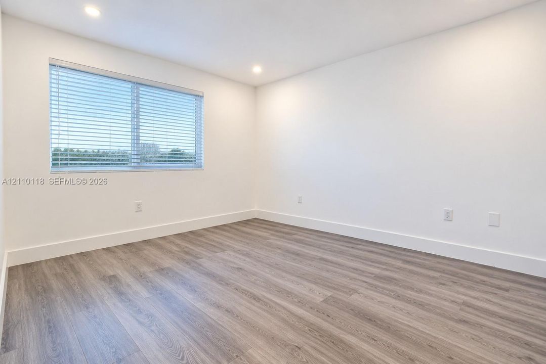 Neutral-toned room featuring wood-finish flooring, recessed lighting, and a single window with horizontal blinds