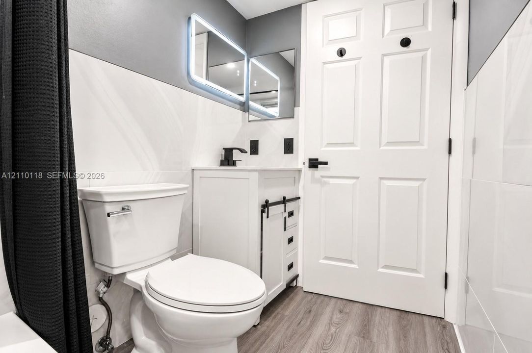 Bathroom featuring a white vanity cabinet with black sliding barn-door hardware, an integrated sink with a matte black faucet, a rectangular LED-backlit mirror, and wood-finish flooring
