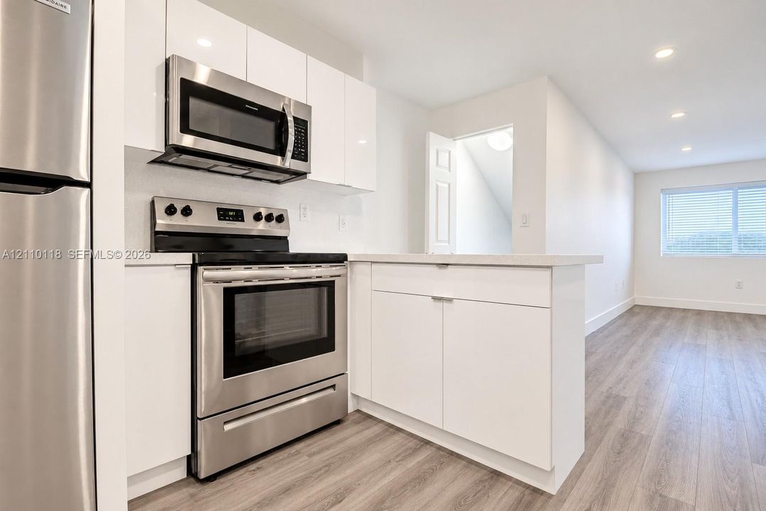 Kitchen featuring white flat-panel cabinetry, stainless steel appliances, solid-surface countertops, and wood-finish flooring with recessed lighting