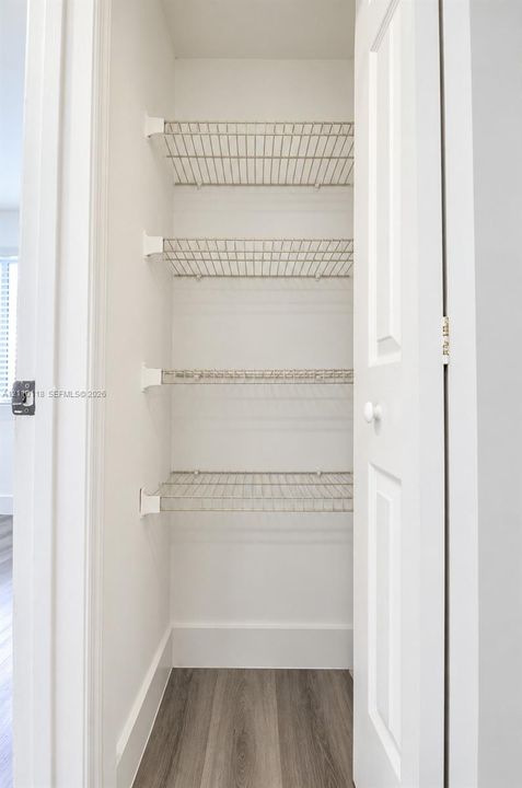 Storage closet featuring white-painted walls, four tiers of wire shelving, and wood-finish flooring