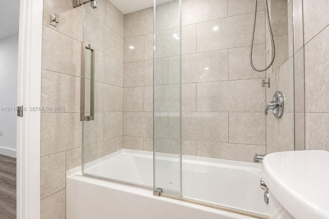 Full-height neutral wall tiling, integrated glass shower screen, chrome plumbing fixtures, and a white soaking tub