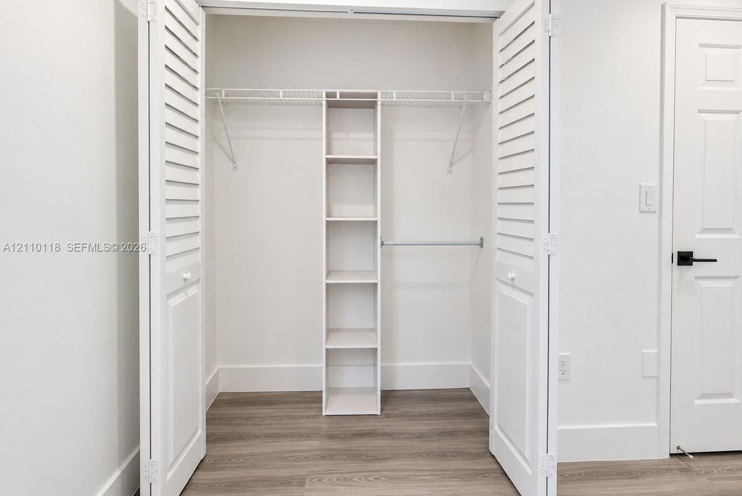 Closet featuring white louvered bifold doors, integrated shelving unit, wire hanging racks, and wood-finish flooring