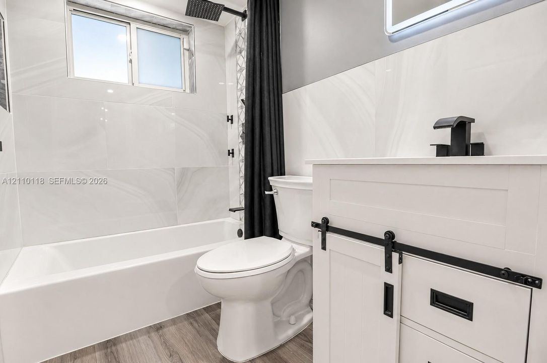 Bathroom featuring large-format wall tile, wood-finish flooring, a white vanity with matte black hardware, and a rainfall showerhead