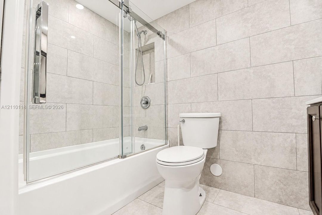 Full-height wall tiling, glass sliding shower enclosure, recessed shower niche, tub-shower combination, and polished chrome fixtures