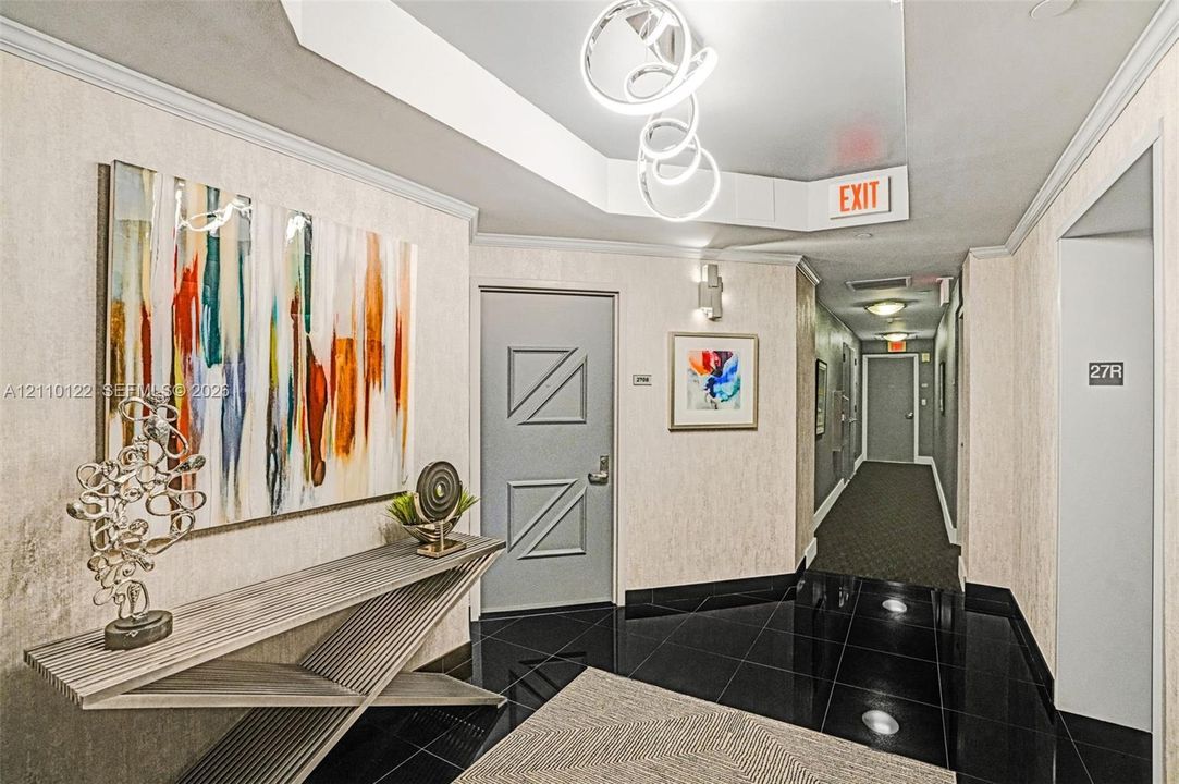 Foyer featuring black tiled flooring, a recessed tray ceiling with sculptural pendant lighting, and textured wall coverings