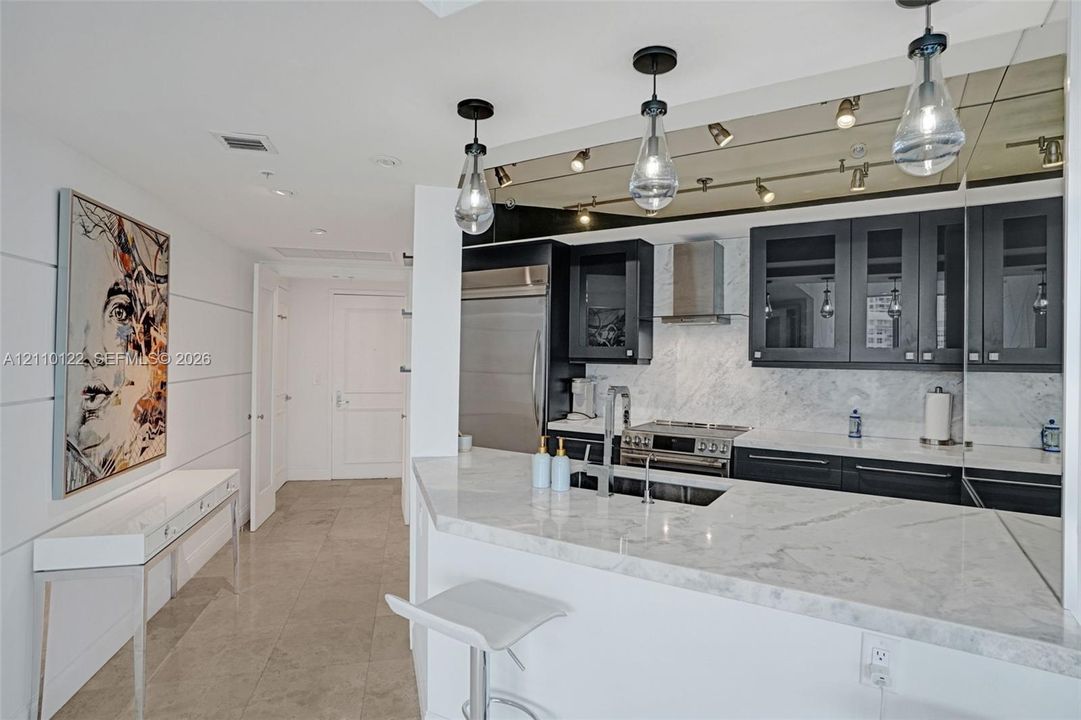 Kitchen featuring stone countertops, dark-finished cabinetry with glass-panel inserts, stainless steel appliances, and teardrop pendant lighting
