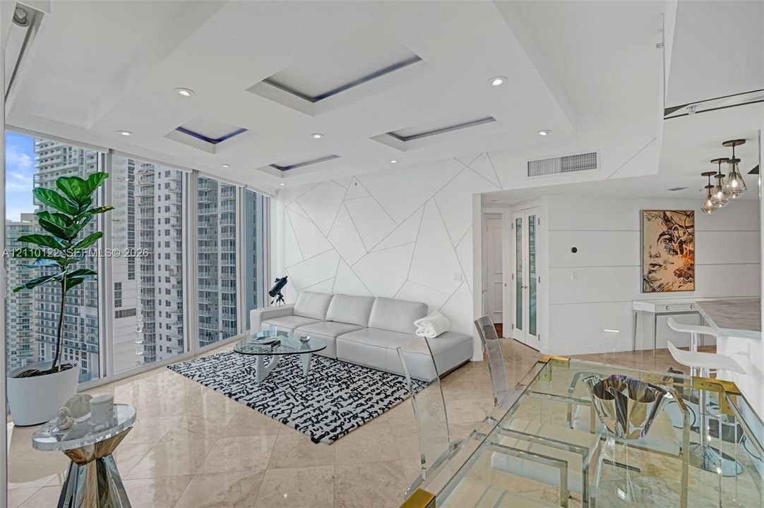 Open-concept living area featuring floor-to-ceiling windows, polished stone flooring, recessed tray ceiling lighting, and a custom geometric wall treatment