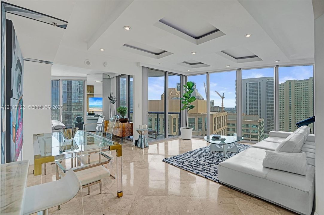 Living space featuring floor-to-ceiling windows, polished stone flooring, recessed tray ceiling detailing, and integrated lighting
