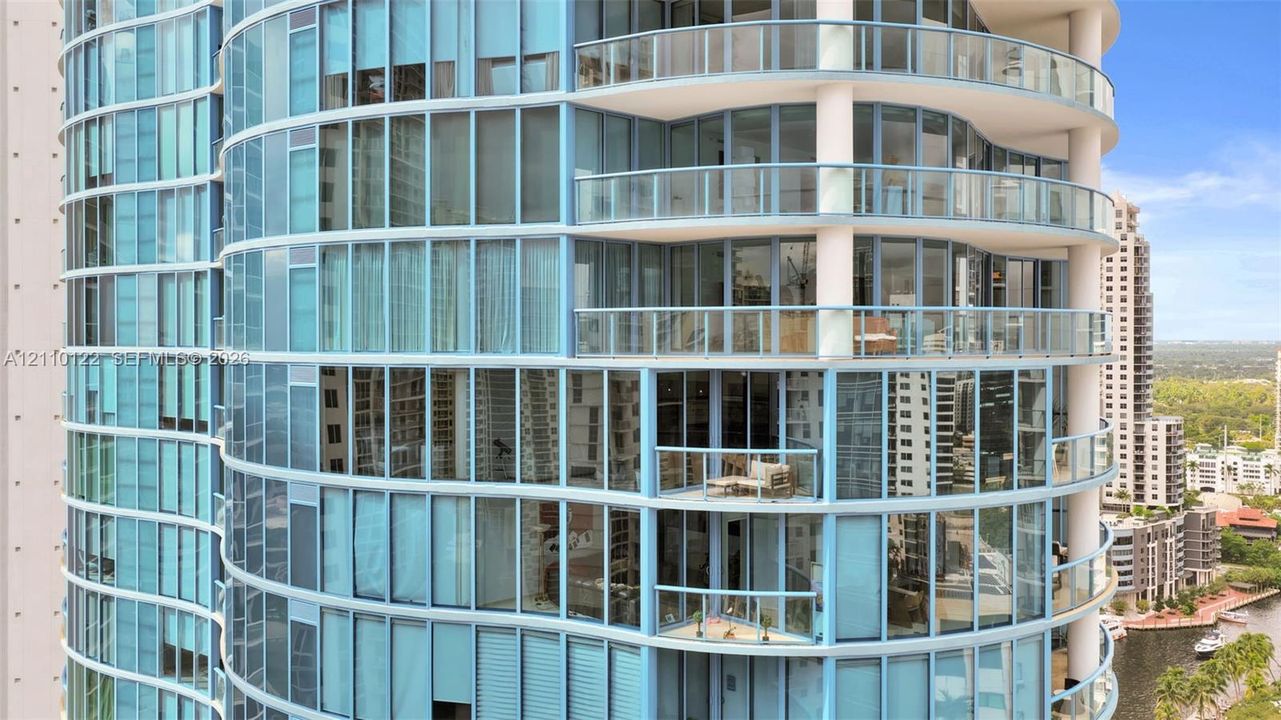 Curved glass facade featuring floor-to-ceiling windows, wrap-around balconies, and glass-paneled railings