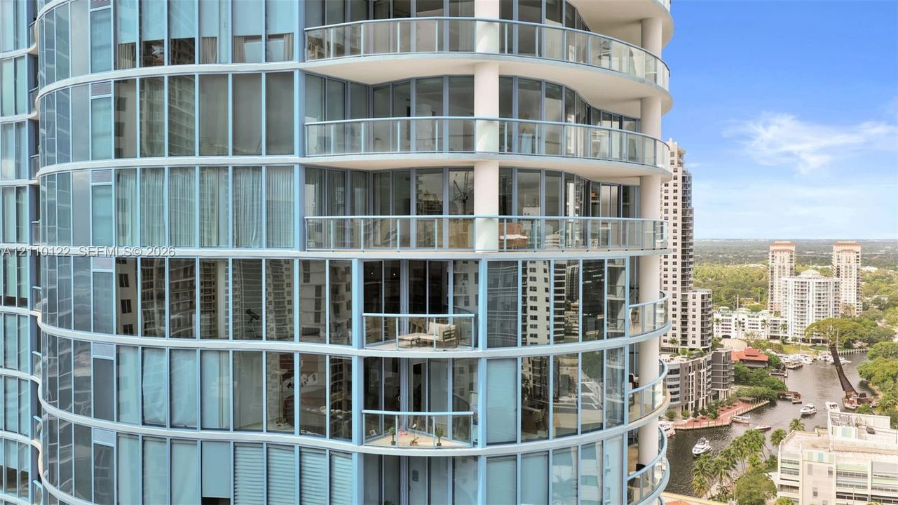 High-rise exterior featuring a rounded architectural facade, floor-to-ceiling glass windows, and multiple private balconies with glass railings