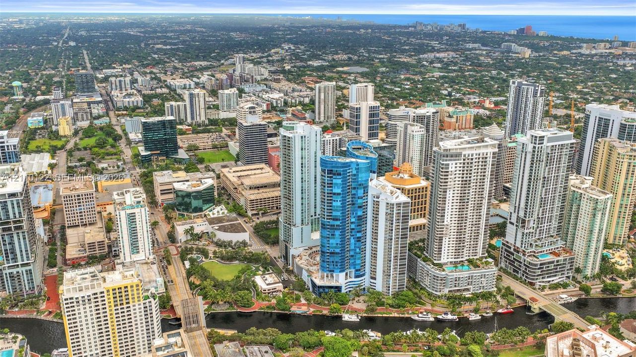 Aerial perspective of a high-density urban environment featuring skyscraper architecture, proximity to a waterway, integrated green spaces, and dense metropolitan infrastructure