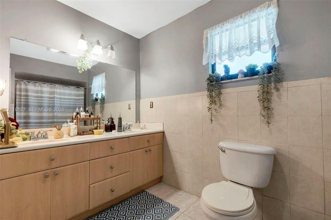 Bathroom featuring a wood-finish vanity with a light-toned countertop, large wall-mounted mirror, three-light fixture, and neutral wall tiling