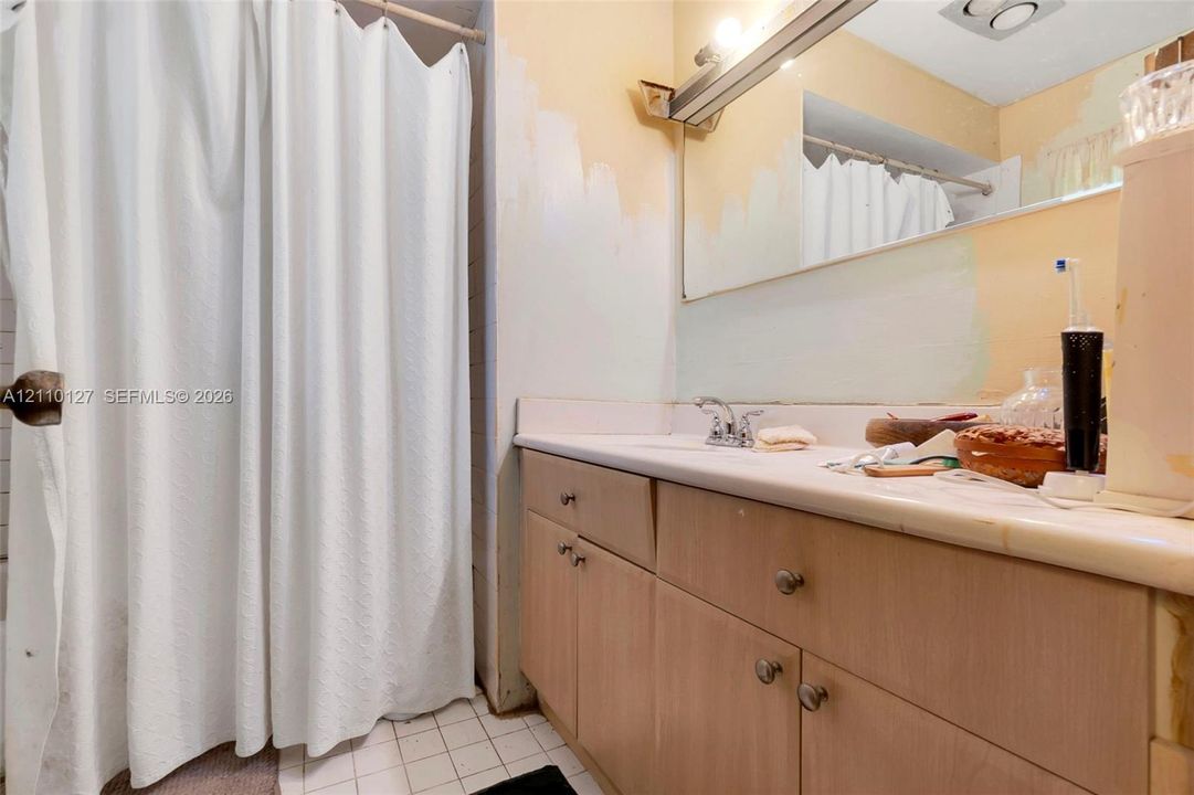 Bathroom featuring a vanity with light-tone wood-finish cabinetry, a solid-surface countertop with an integrated sink, a large wall-mounted mirror, and a shower area with a curtain rod