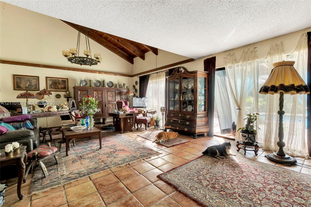 Living area featuring a vaulted ceiling with exposed wood beams, ceramic tile flooring, and sliding glass doors