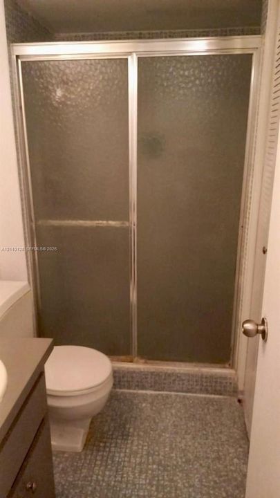 Shower stall featuring a metal-framed enclosure with textured privacy glass and a tiled floor, accompanied by a built-in vanity cabinet and standard porcelain toilet