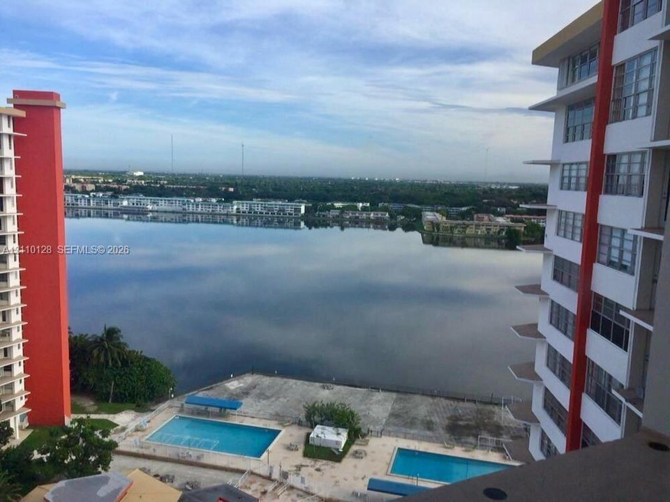 High-rise exterior with dual swimming pools and concrete pool deck, centered on a large lake expanse