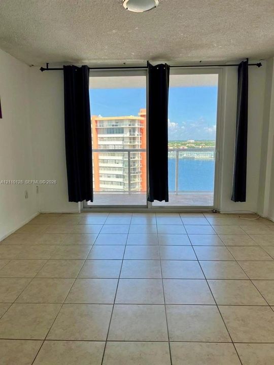 Floor-to-ceiling sliding glass doors opening to a balcony with a glass railing and ceramic tile flooring