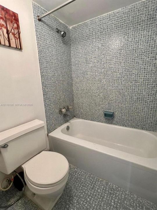 Bathroom featuring a porcelain bathtub, integrated shower fixture with curtain rod, patterned mosaic wall tiling, and a built-in soap dish