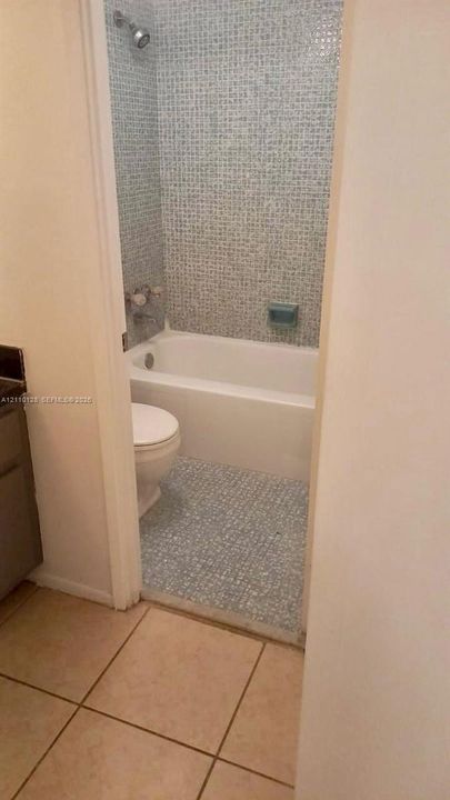 Bathroom featuring blue mosaic wall tile, a white porcelain soaking tub, a built-in soap niche, and light-toned floor tiling
