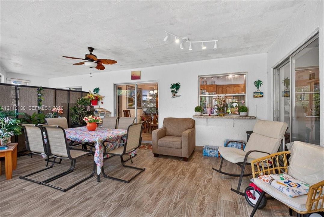 Enclosed patio featuring wood-finish flooring, a ceiling fan, multi-light track lighting, and a passthrough window with a stone-top ledge