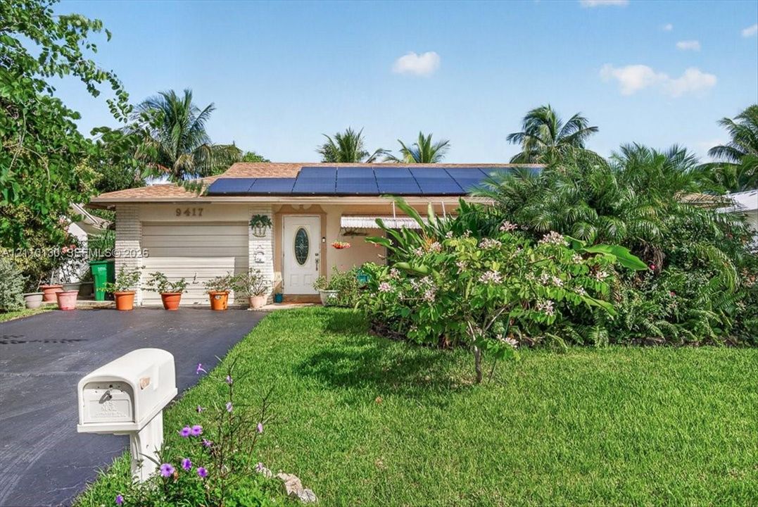 Single-story residence featuring a roof-mounted solar panel system, brick veneer exterior, attached one-car garage, and established landscaping