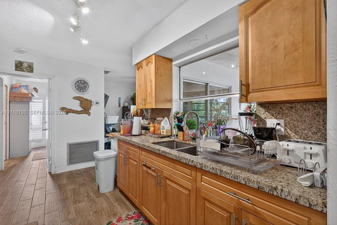 Kitchen featuring natural wood cabinetry, stone-finish countertops, dual-basin stainless steel sink with a high-arch pull-down faucet, and wood-finish tile flooring