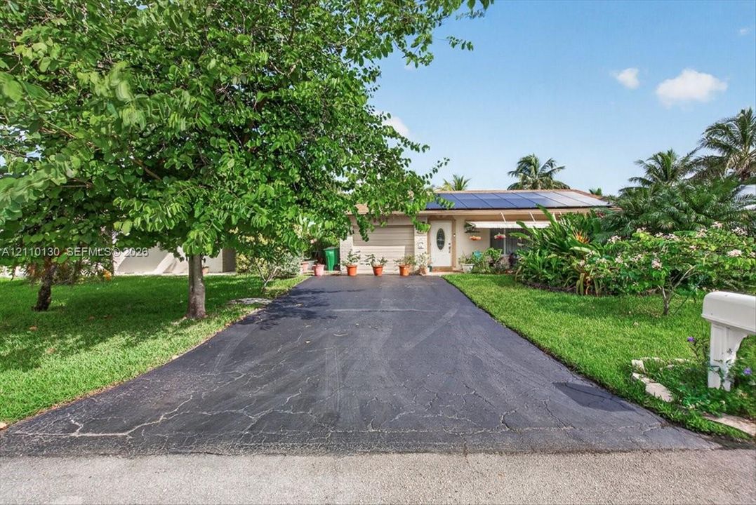 Single-story residence featuring an asphalt driveway, roof-mounted solar panels, mature landscaping, and an attached garage
