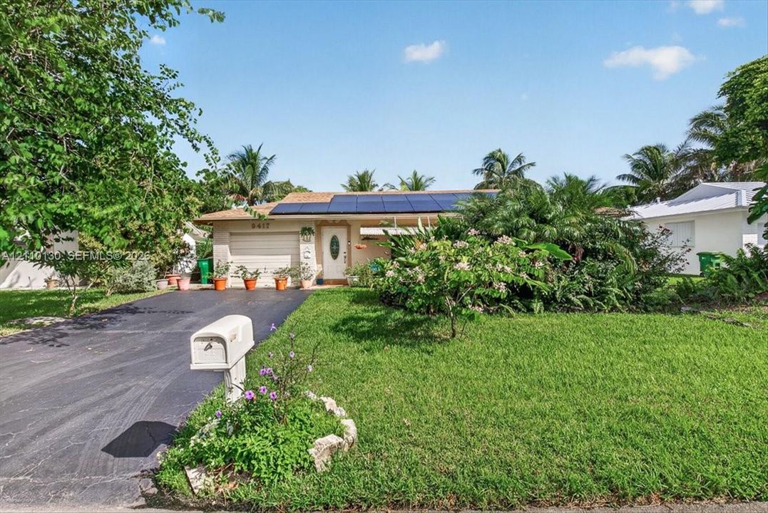Single-story exterior featuring rooftop solar panels, an attached garage, a paved driveway, and established landscaping