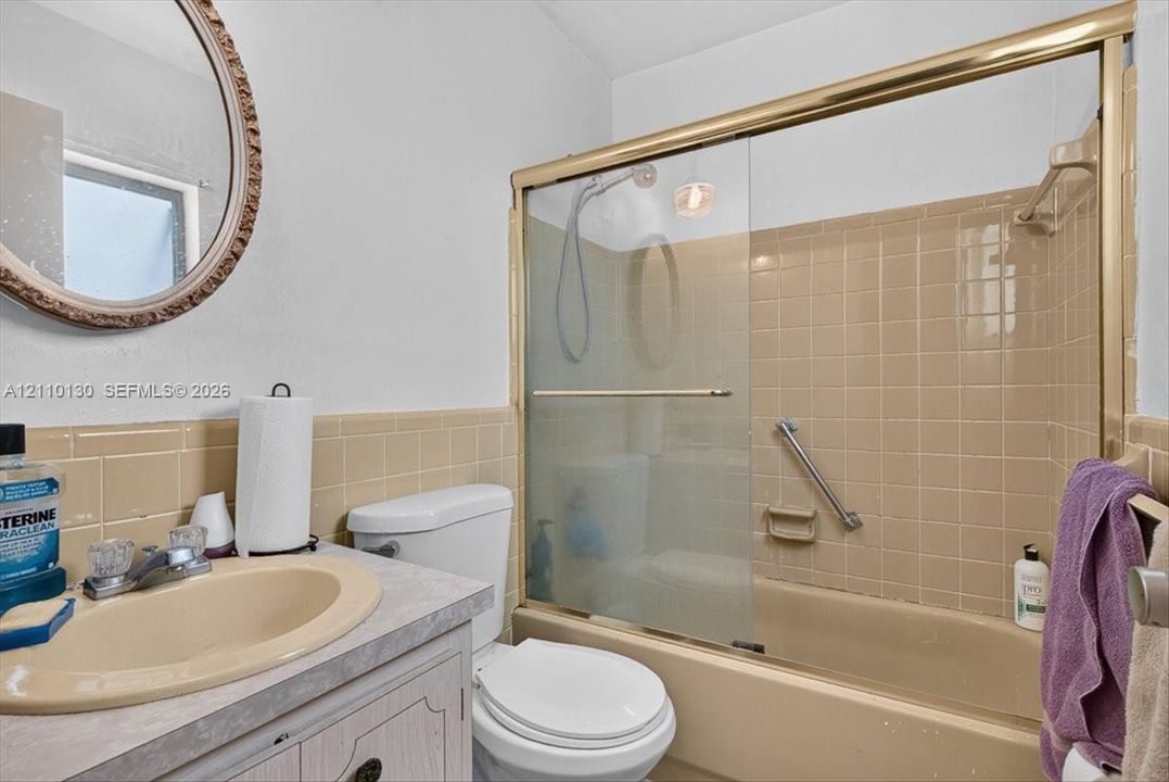 Bathroom featuring a vanity with integrated sink, tub-shower combination with sliding glass doors, brass-finish trim, and ceramic wall tiling