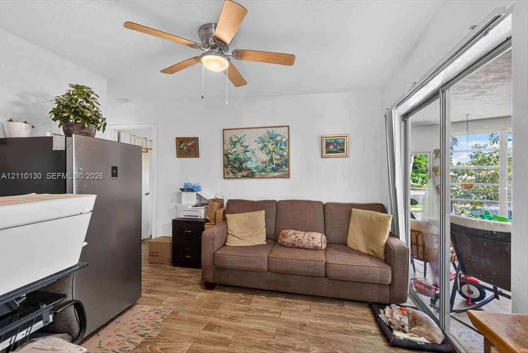 Wood-finish flooring, ceiling fan with integrated lighting, and sliding glass doors providing outdoor access