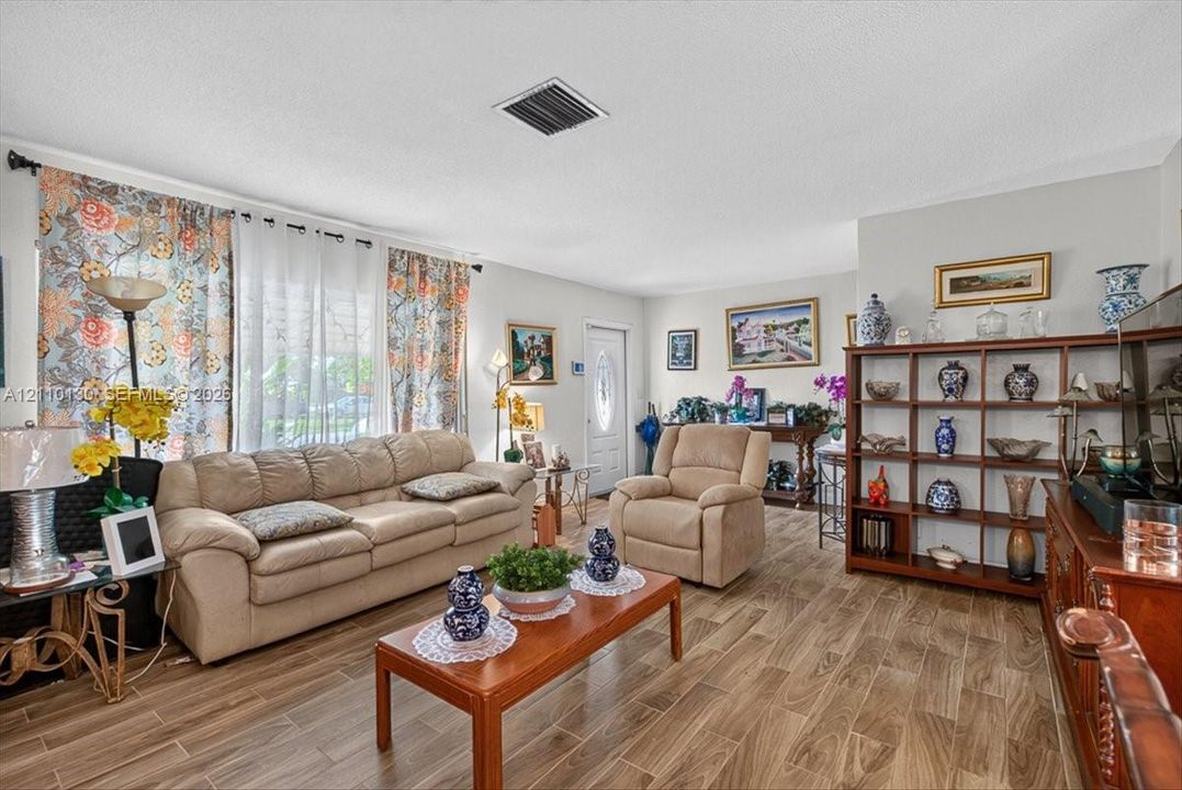 Living area featuring wood-finish tile flooring, neutral wall paint, and a white front entry door with an oval glass insert