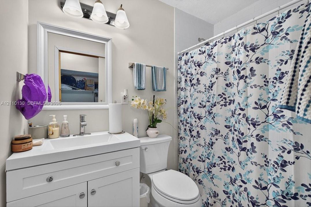 White vanity with integrated rectangular sink, chrome single-handle faucet, framed wall-mounted mirror, three-light overhead fixture, and porcelain toilet
