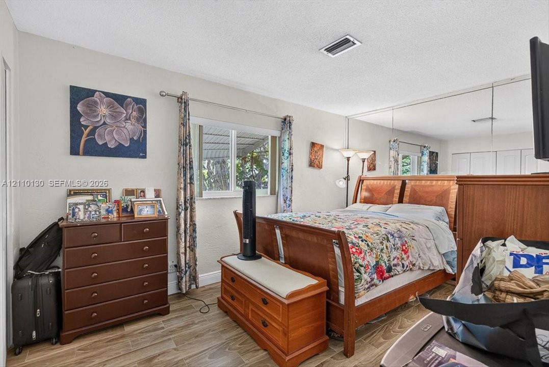 Neutral interior featuring wood-finish flooring, a window with horizontal blinds, and a full-width mirrored wall