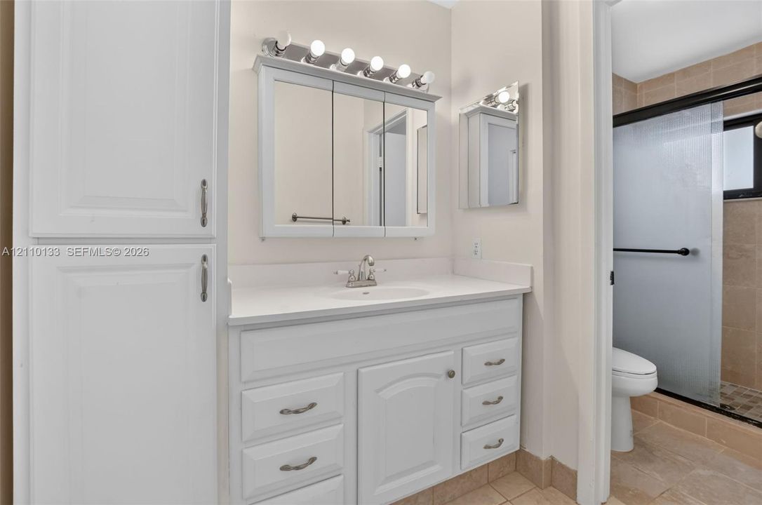 Bathroom featuring a white vanity with integrated cabinetry, solid surface countertop, tri-fold medicine cabinet, and a glass-enclosed shower with tiled surround