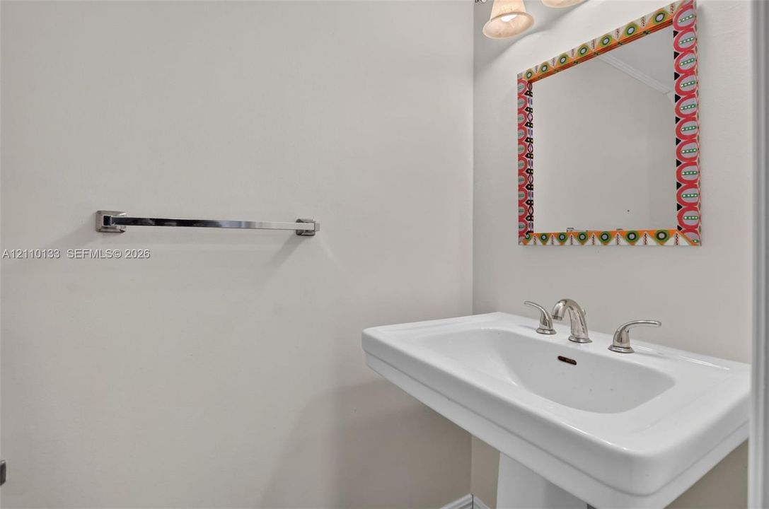 Wall-mounted pedestal sink featuring a widespread polished chrome faucet, polished chrome towel bar, and multi-light vanity fixture