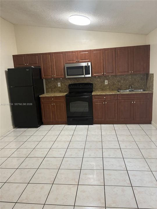 Kitchen featuring wood cabinetry, stone-finish countertops, black appliances, a mounted microwave, and ceramic tile flooring