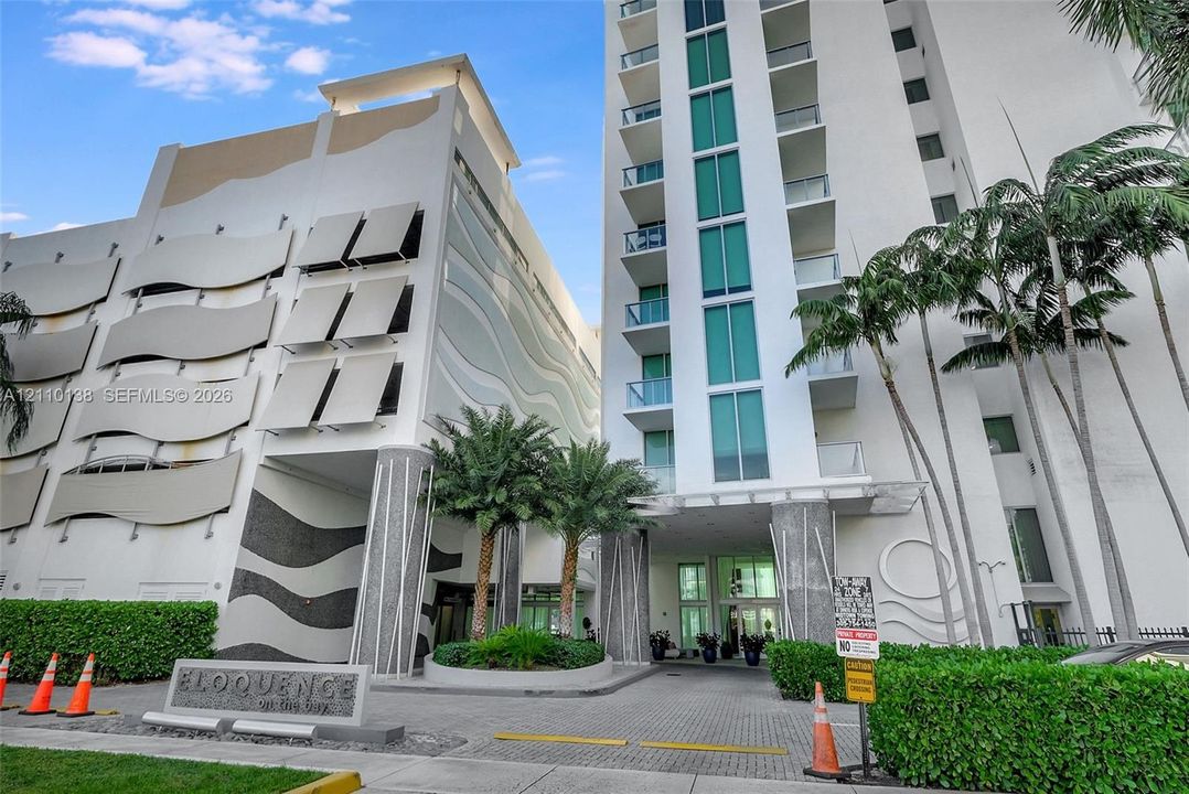 Multi-story high-rise exterior featuring a sculpted facade, private balconies with glass railings, tiered landscaping, and a paver-stone motor court
