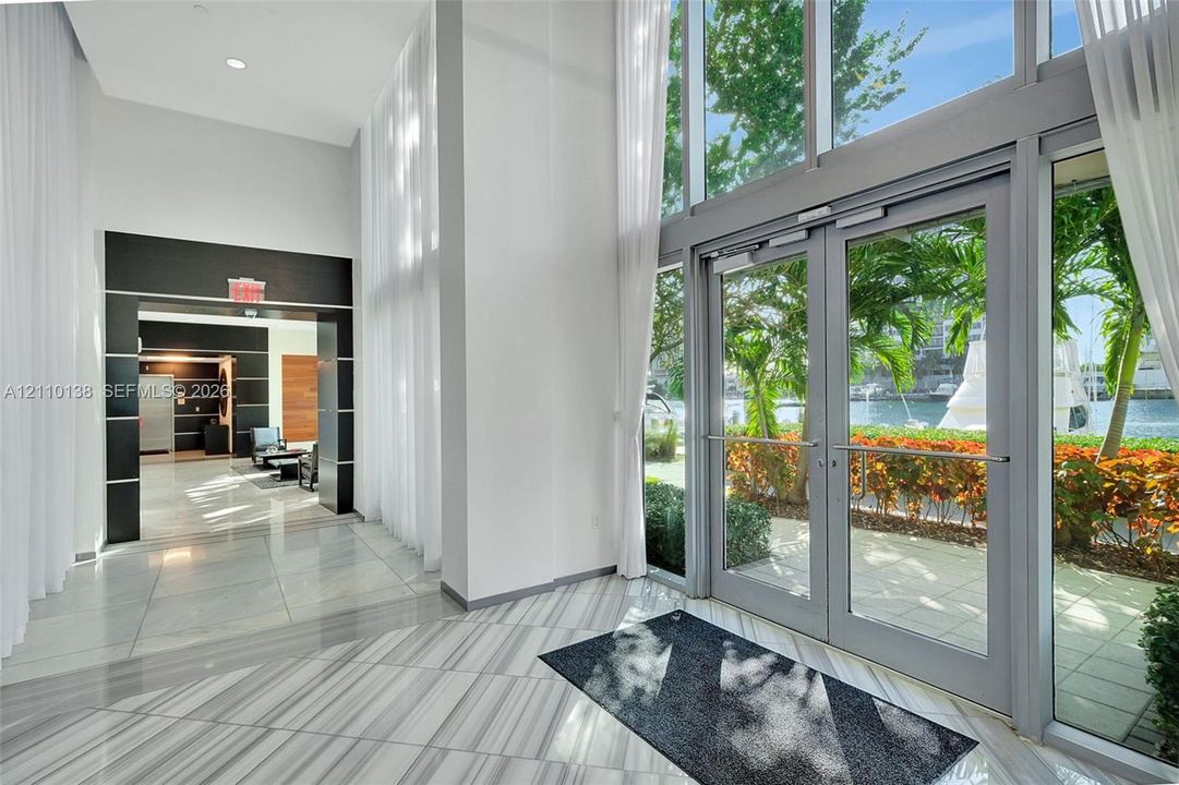 Grand entrance featuring high ceilings, floor-to-ceiling windows, dual-entry glass doors, and polished stone tile flooring