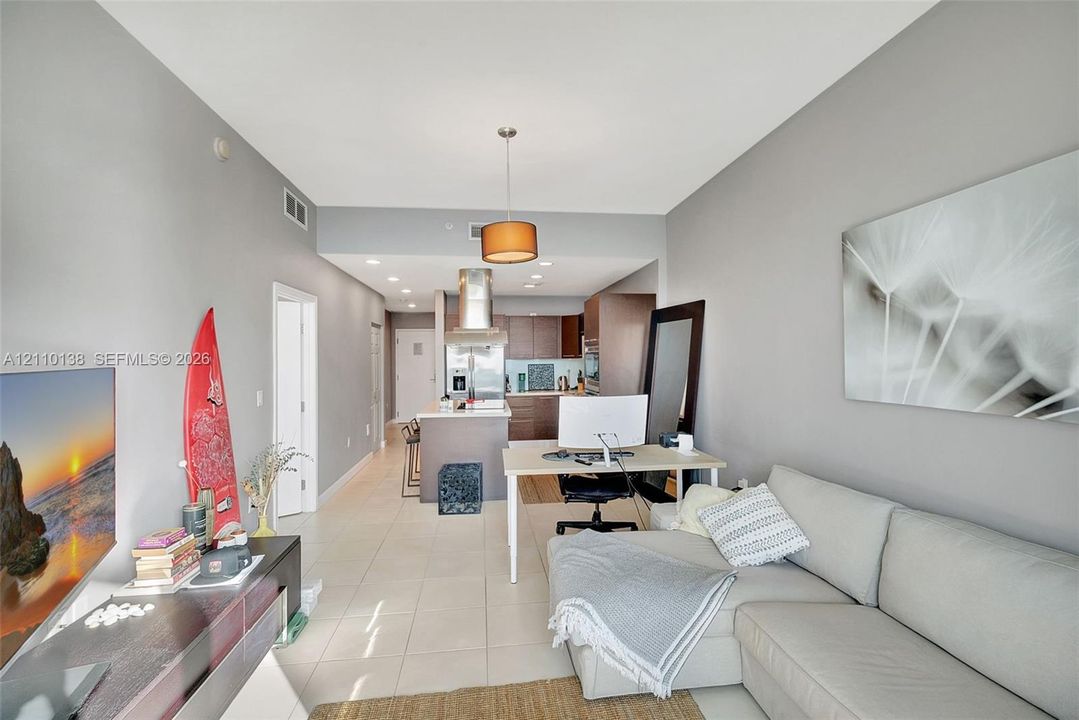 Open-concept interior featuring neutral wall tones, large-format tile flooring, recessed ceiling lighting, and a kitchen equipped with dark-finish cabinetry and a stainless steel range hood